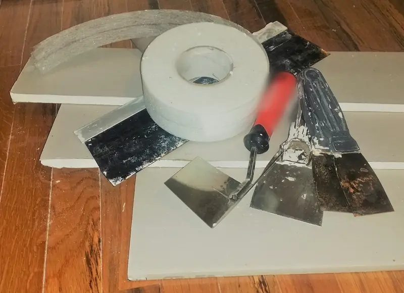 Rouleau de bande à joint et couteaux à enduire posés sur des plaques de plâtre