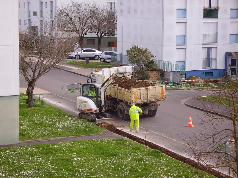 Mini-pelle qui charge la terre dans un camion benne au pied d’un immeuble